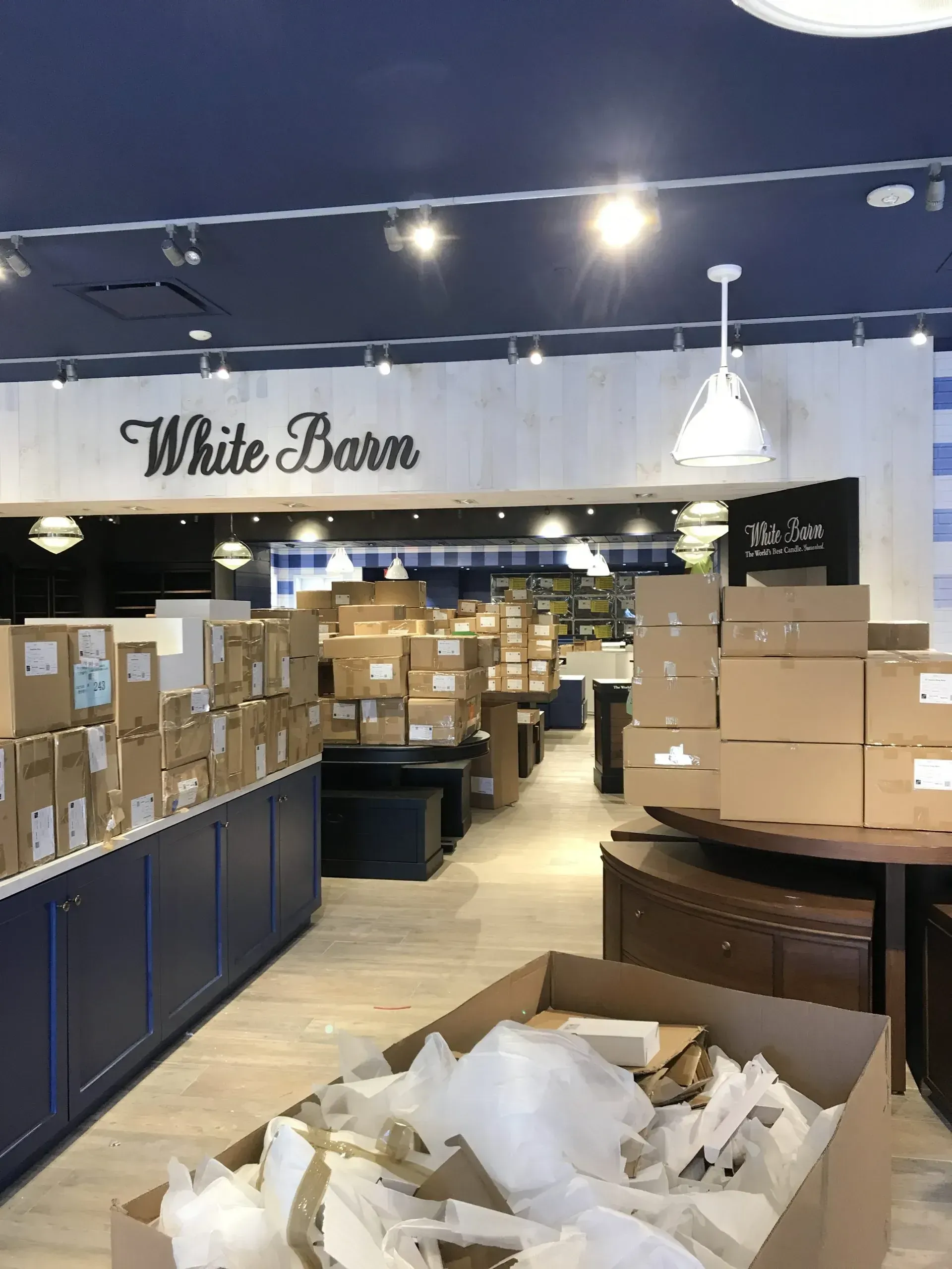 White Barn store interior with unpacked boxes, a blue and white decor, and overhead lighting.