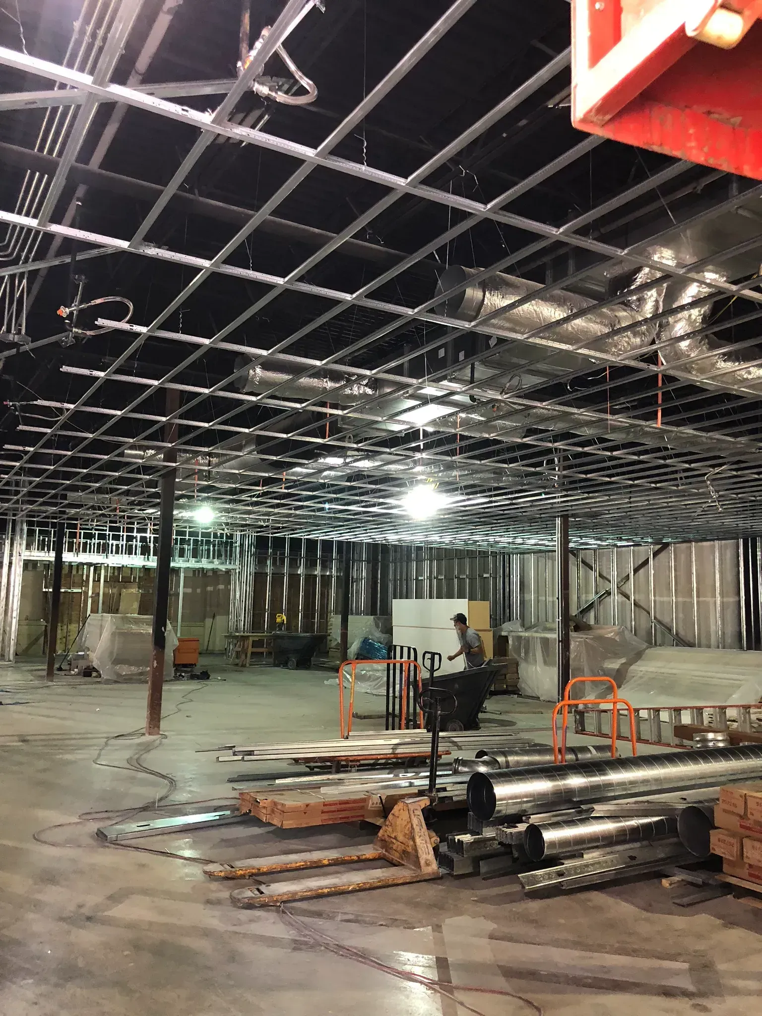 Interior construction site, exposed ceiling grid, drywall, and equipment on concrete floor.
