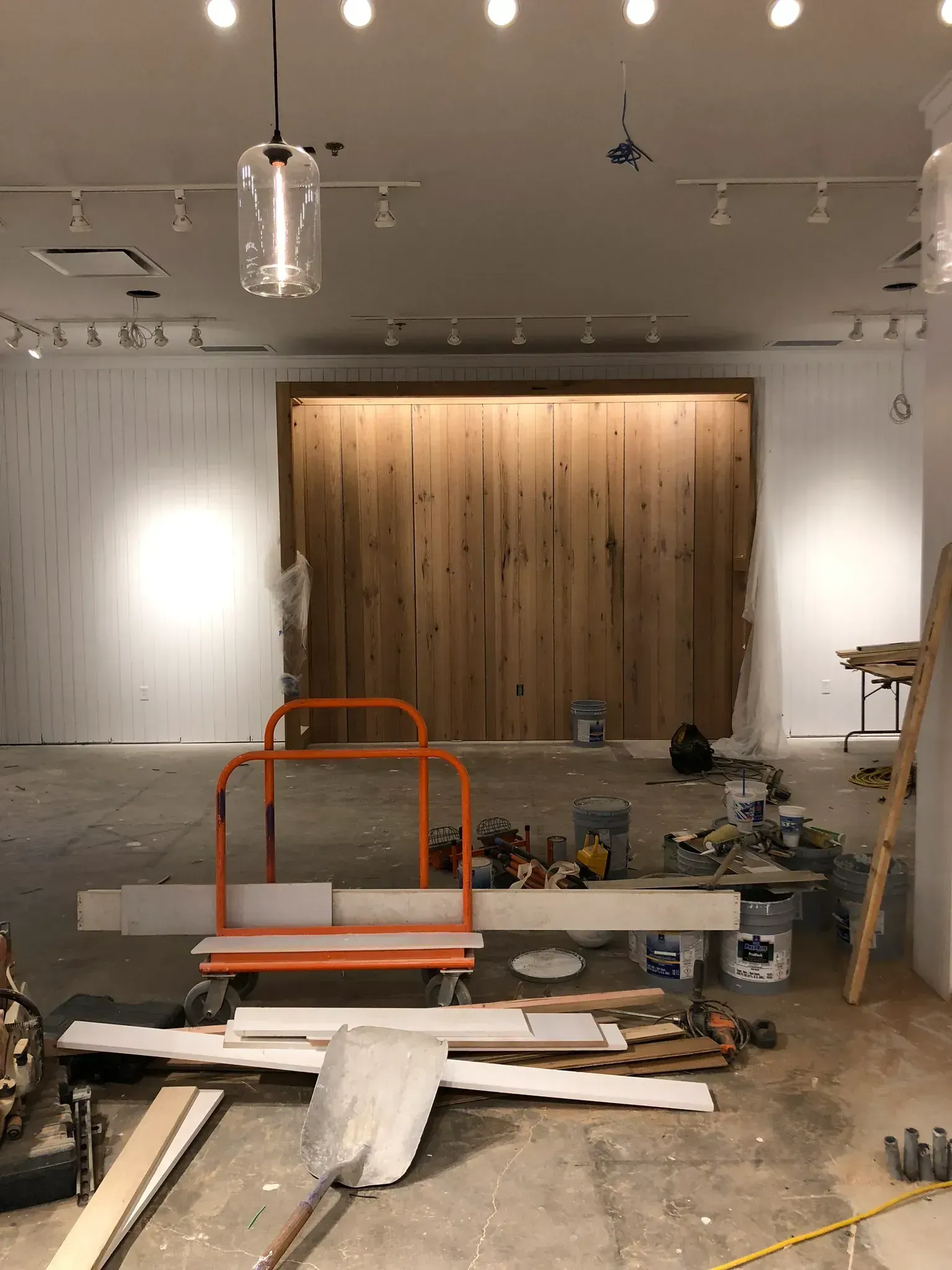 Interior of a store under construction with wooden feature wall, exposed concrete floor, and construction equipment.