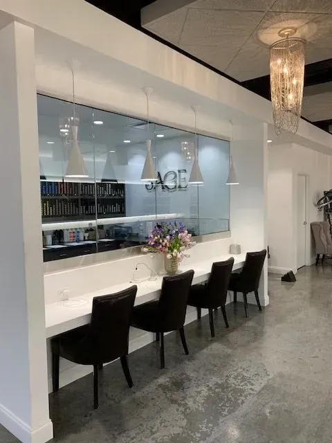 Row of dark chairs at a white counter in a modern space, with a window and pendant lights overhead.