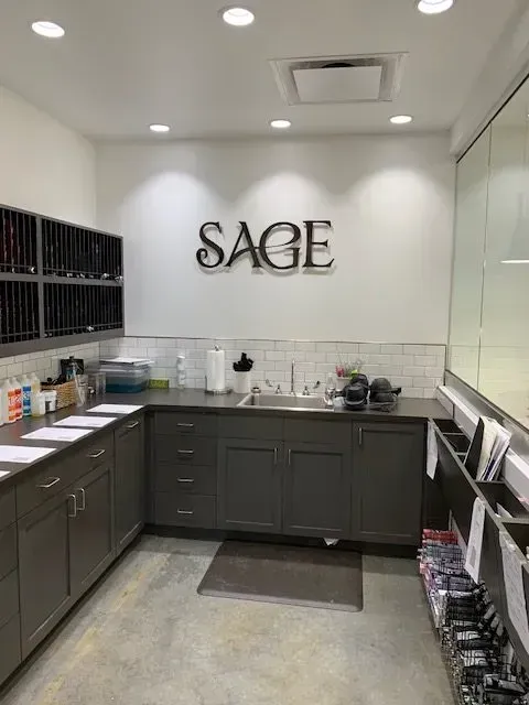 Sage salon work area with cabinets, sink, and storage shelves. The word "SAGE" is on the wall.