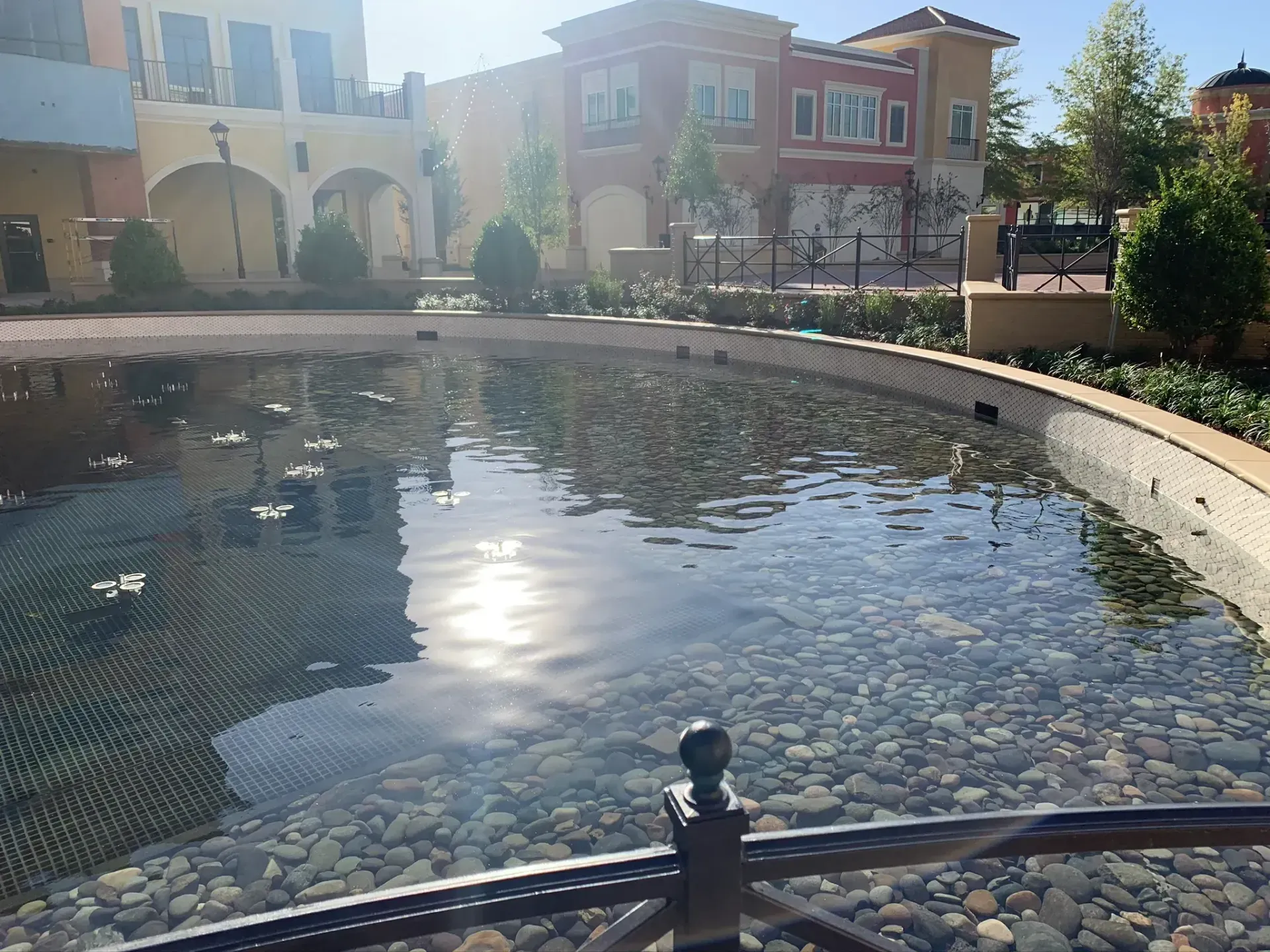 Pond with clear water reflecting sunlight, surrounded by buildings with colorful facades.