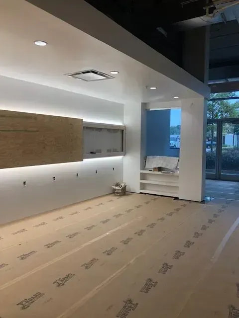 Interior of a room under construction with white walls, recessed lighting, and protective floor covering.